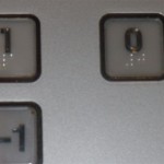 Widok przycisków windzie z oznaczeniami brajlowskimi.